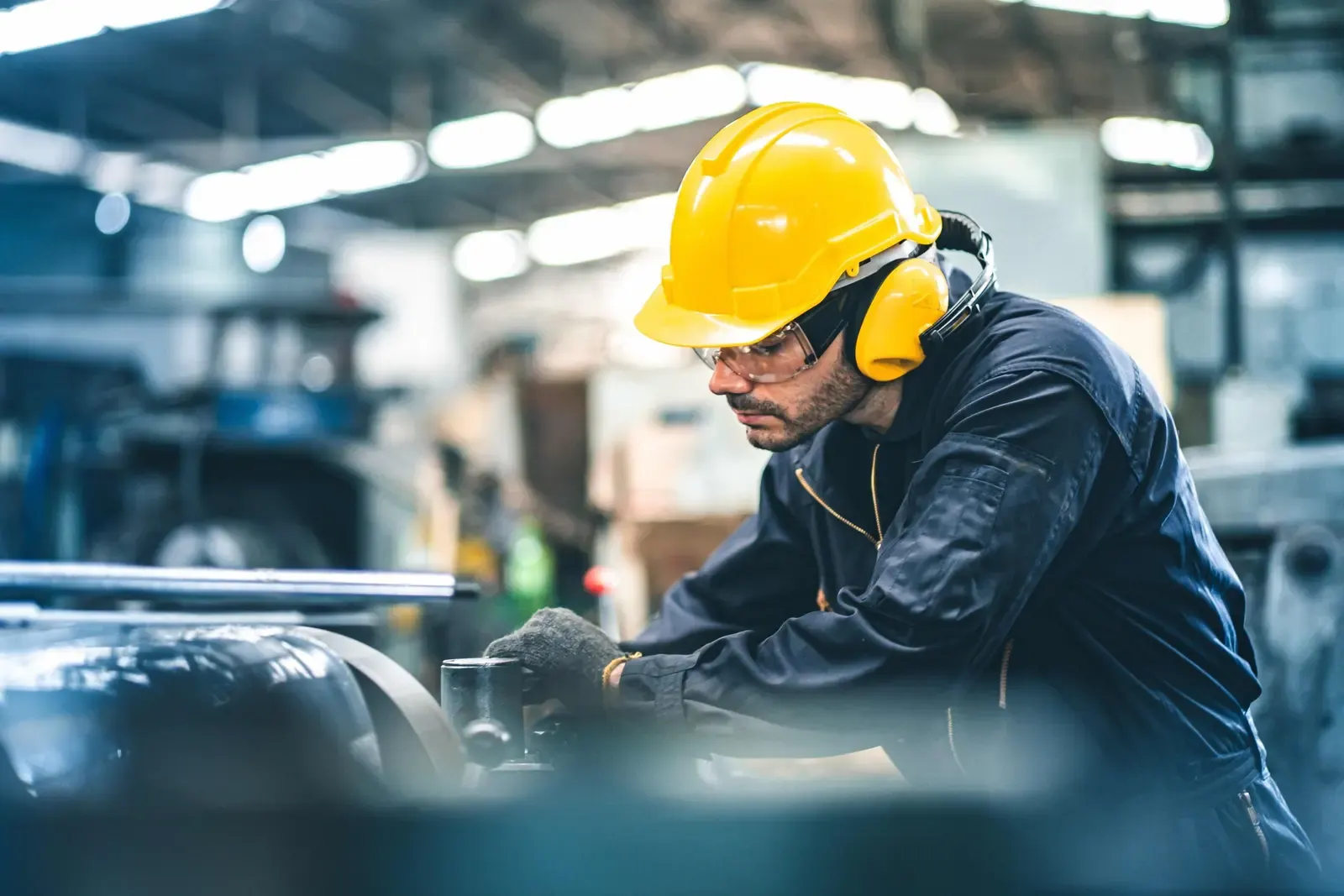Trabalhador com capacete, óculos e protetor auricular opera equipamento em ambiente industrial